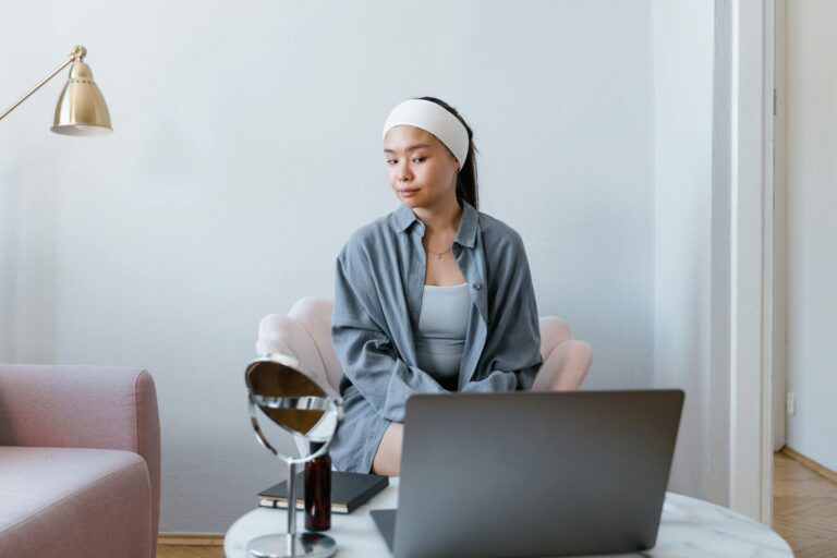 Asian woman sitting in living room with laptop doing beauty routine.
