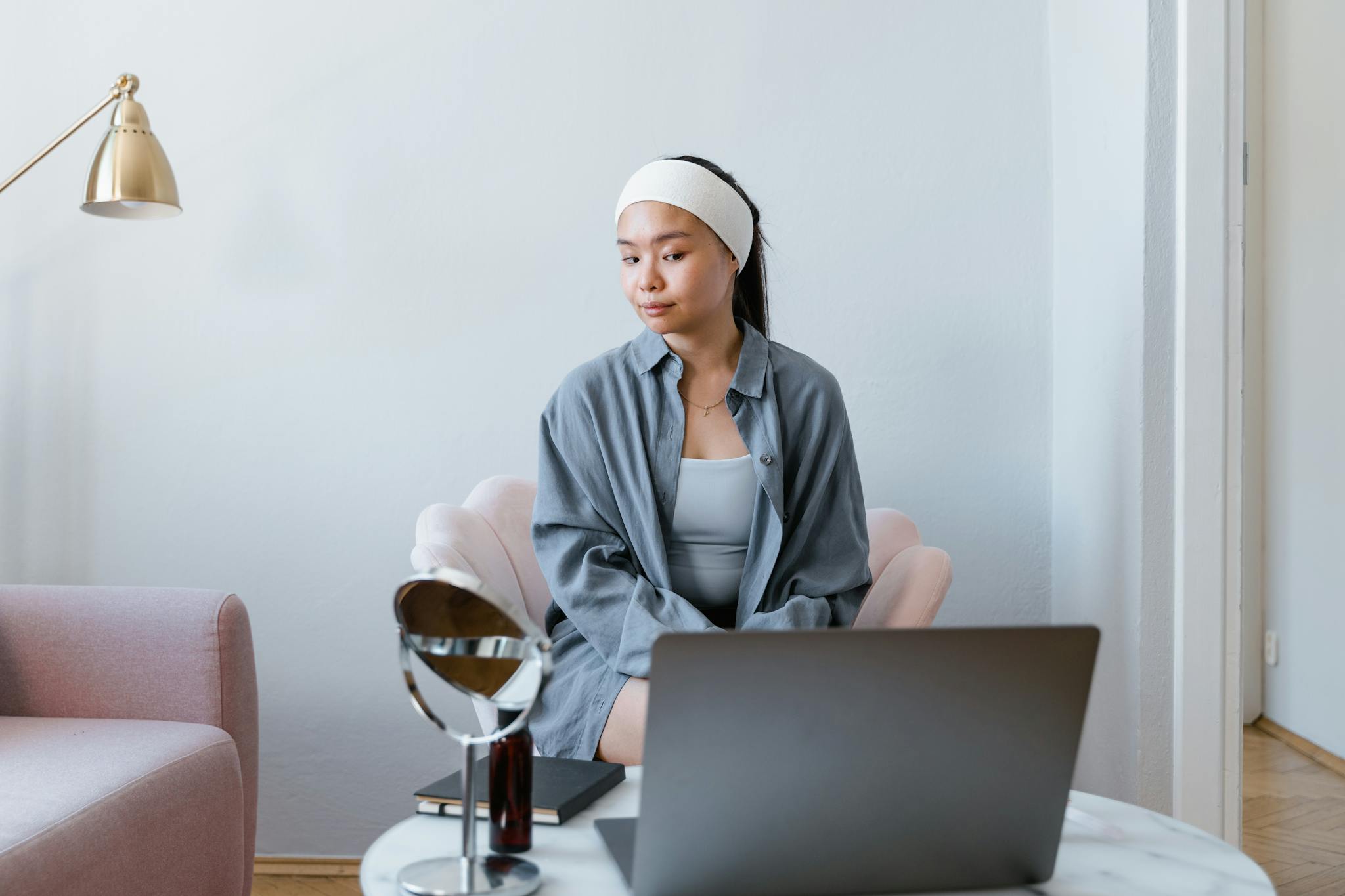 Asian woman sitting in living room with laptop doing beauty routine.